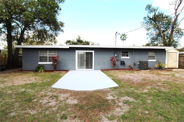 rear view of property featuring cooling unit, concrete block siding, a storage shed, and a patio