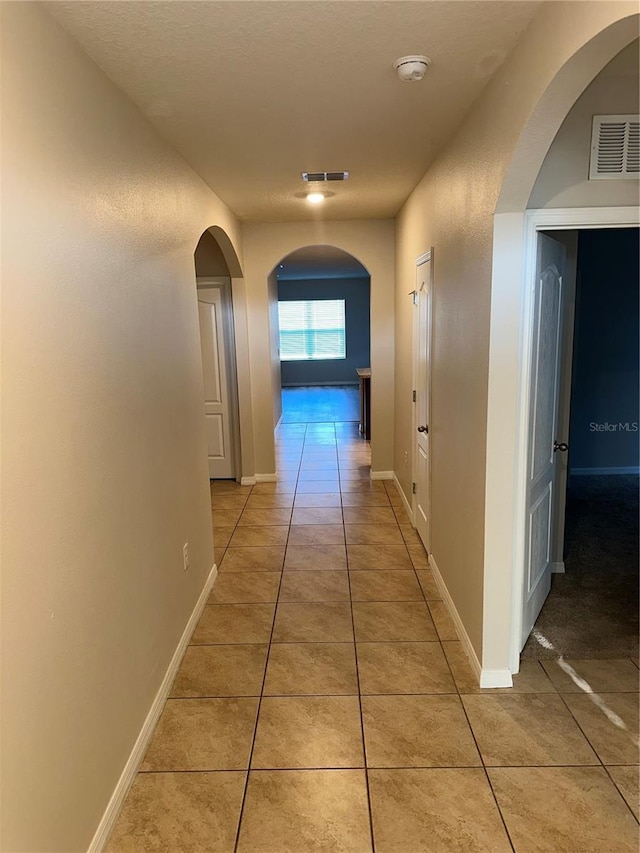 hallway with light tile patterned floors, visible vents, baseboards, and arched walkways