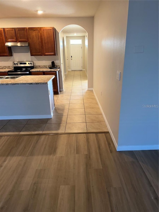 kitchen with baseboards, light wood-style flooring, arched walkways, light countertops, and electric stove