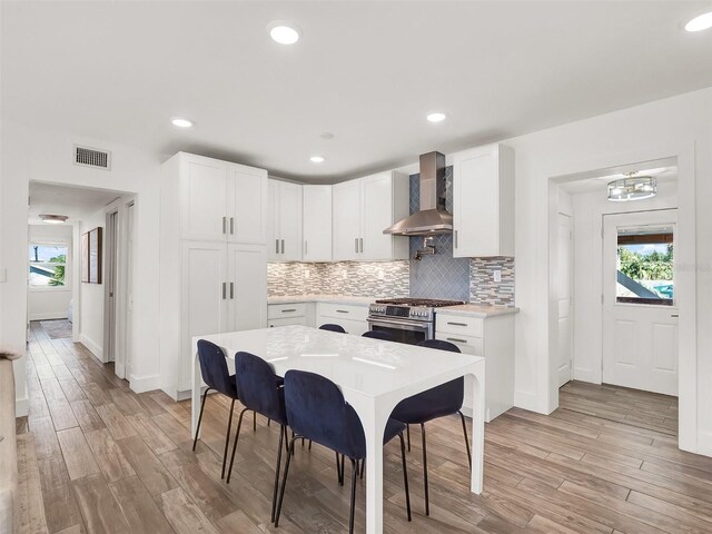 kitchen with tasteful backsplash, visible vents, high end stove, light wood finished floors, and wall chimney exhaust hood