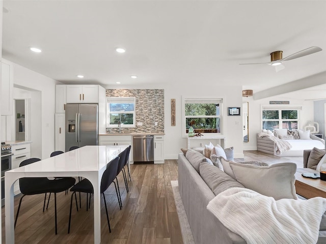 kitchen with open floor plan, light wood-style floors, appliances with stainless steel finishes, decorative backsplash, and a healthy amount of sunlight