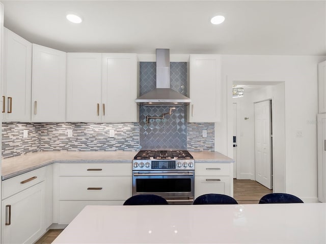 kitchen featuring stainless steel range with gas cooktop, decorative backsplash, light countertops, white cabinets, and wall chimney exhaust hood