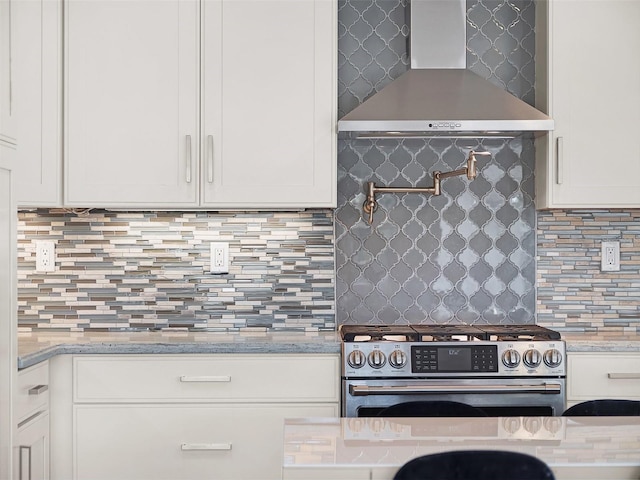 kitchen with stainless steel gas range oven, decorative backsplash, white cabinets, and wall chimney range hood