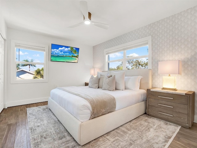 bedroom with multiple windows, wallpapered walls, baseboards, and wood finished floors