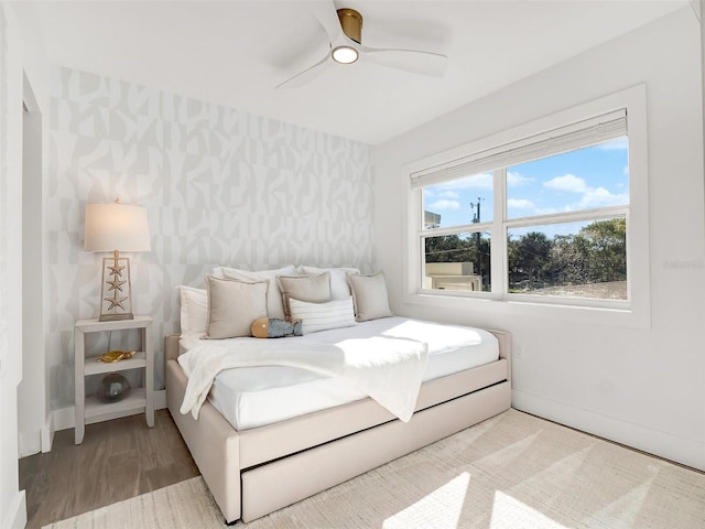 bedroom with wallpapered walls, wood finished floors, baseboards, and ceiling fan