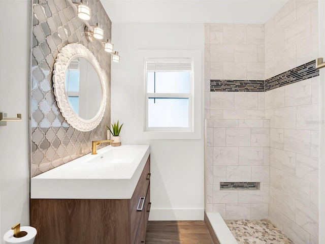 bathroom featuring a tile shower, vanity, baseboards, and wood finished floors