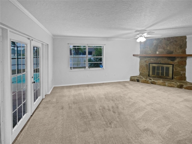 unfurnished living room with ceiling fan, ornamental molding, carpet flooring, a stone fireplace, and a textured ceiling