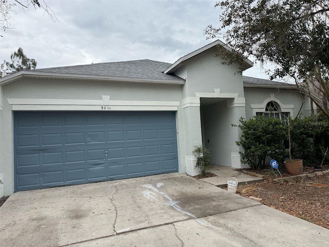 ranch-style house with concrete driveway, an attached garage, roof with shingles, and stucco siding