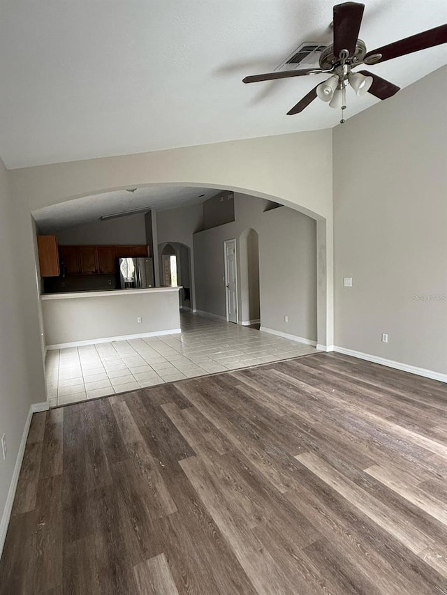 unfurnished living room with vaulted ceiling, light wood-style flooring, a ceiling fan, and arched walkways