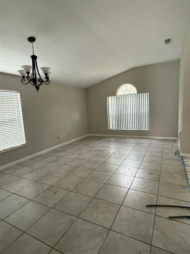 tiled empty room with lofted ceiling, baseboards, visible vents, and a chandelier