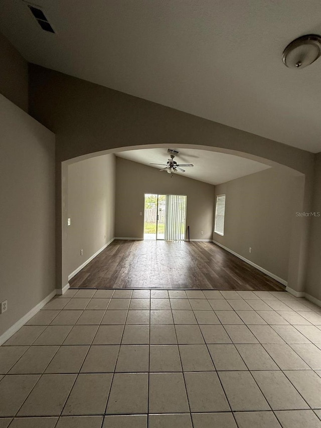 unfurnished room featuring a ceiling fan, baseboards, lofted ceiling, light tile patterned flooring, and arched walkways