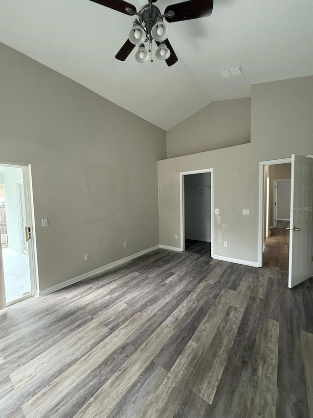 unfurnished bedroom with high vaulted ceiling, a walk in closet, baseboards, and dark wood-style flooring