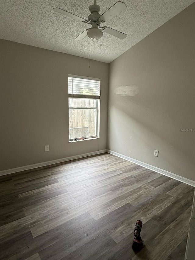 spare room with a textured ceiling, a ceiling fan, baseboards, and dark wood-style flooring