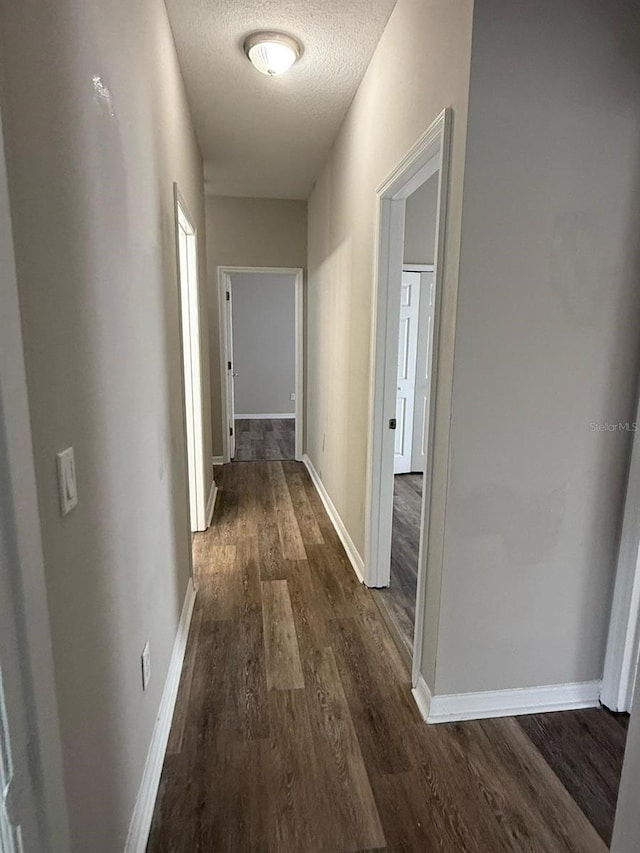 hall with baseboards, dark wood-type flooring, and a textured ceiling