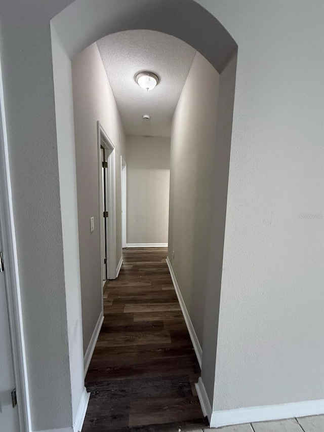 hallway featuring wood finished floors, baseboards, arched walkways, and a textured ceiling