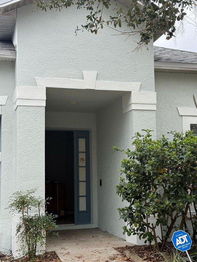 property entrance with roof with shingles and stucco siding