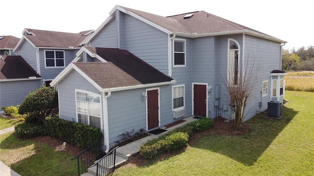 traditional-style home featuring central AC unit, a front yard, and roof with shingles