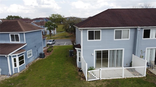 back of house featuring a lawn, a shingled roof, and central AC