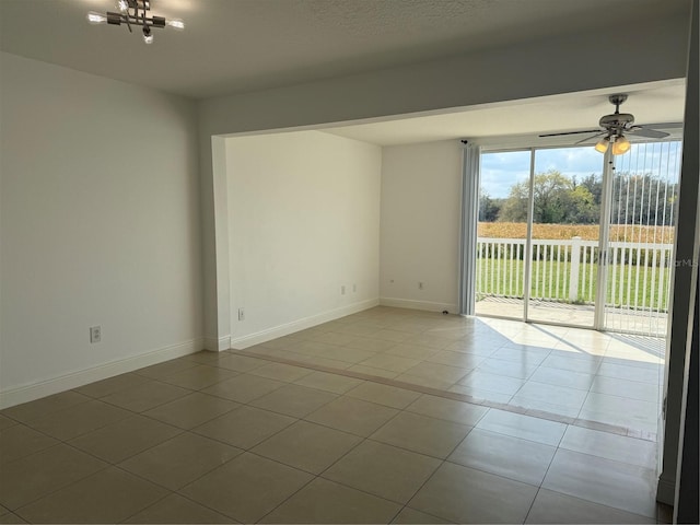 empty room with tile patterned floors, ceiling fan with notable chandelier, and baseboards