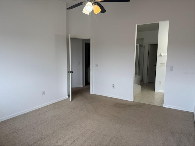 unfurnished bedroom with connected bathroom, baseboards, light colored carpet, light tile patterned floors, and a ceiling fan