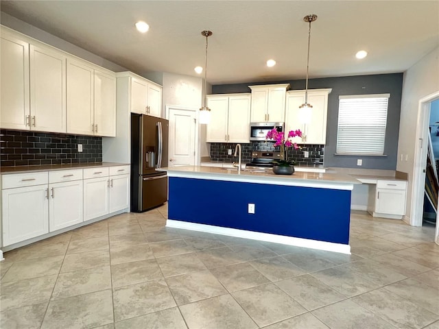 kitchen featuring an island with sink, a sink, hanging light fixtures, white cabinets, and appliances with stainless steel finishes