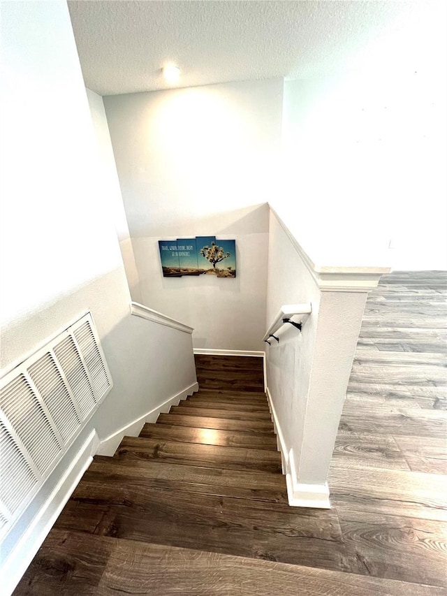 staircase with visible vents, a textured ceiling, baseboards, and wood finished floors