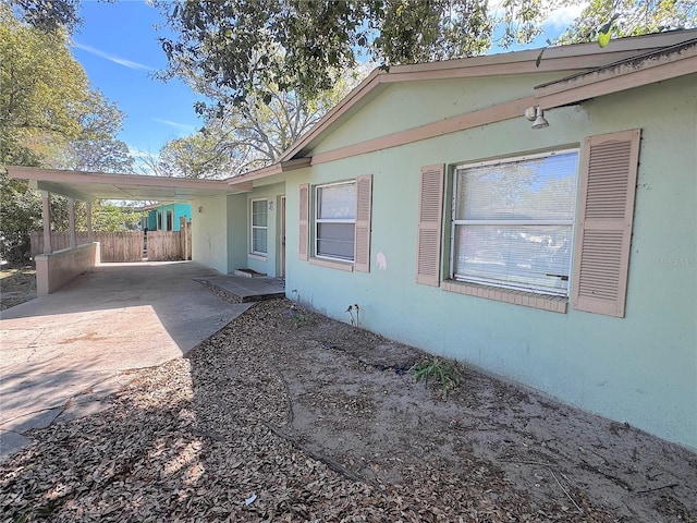 back of house with stucco siding, an attached carport, driveway, and fence