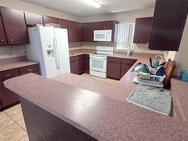 kitchen with dark brown cabinetry, light countertops, a peninsula, light tile patterned flooring, and white appliances