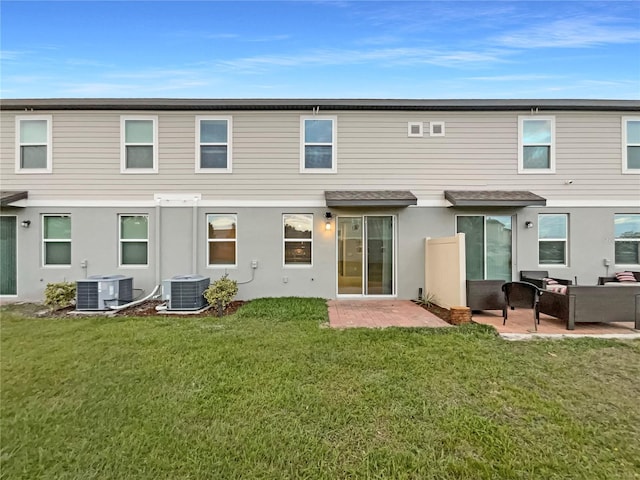 rear view of property with central air condition unit, a lawn, stucco siding, and a patio area