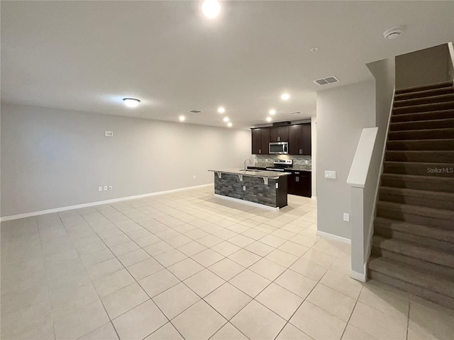 kitchen with a sink, tasteful backsplash, open floor plan, stainless steel appliances, and light tile patterned flooring