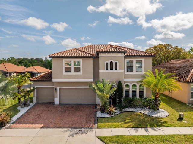 mediterranean / spanish home featuring a front lawn, fence, a tile roof, stucco siding, and decorative driveway