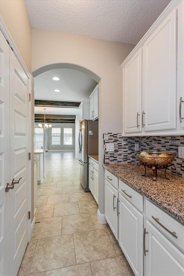 kitchen with stone counters, arched walkways, freestanding refrigerator, white cabinetry, and tasteful backsplash