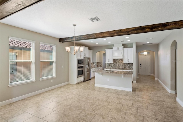 kitchen featuring beam ceiling, appliances with stainless steel finishes, tasteful backsplash, and arched walkways