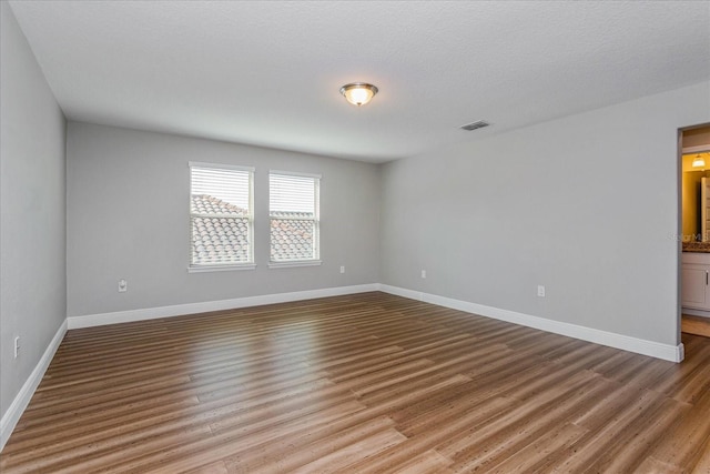 unfurnished room featuring visible vents, baseboards, a textured ceiling, and wood finished floors