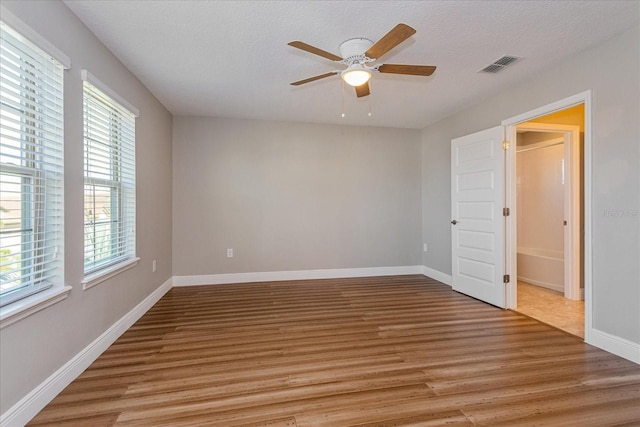 empty room featuring visible vents, a ceiling fan, a textured ceiling, light wood finished floors, and baseboards