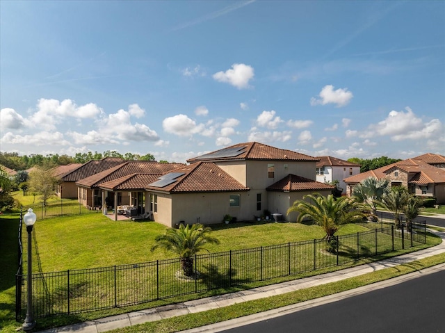 mediterranean / spanish house featuring solar panels, a tiled roof, a front lawn, and a fenced backyard