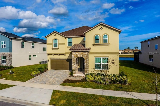 mediterranean / spanish home featuring decorative driveway, stone siding, a front yard, and stucco siding