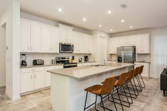 kitchen with a sink, white cabinetry, appliances with stainless steel finishes, a breakfast bar area, and a large island with sink