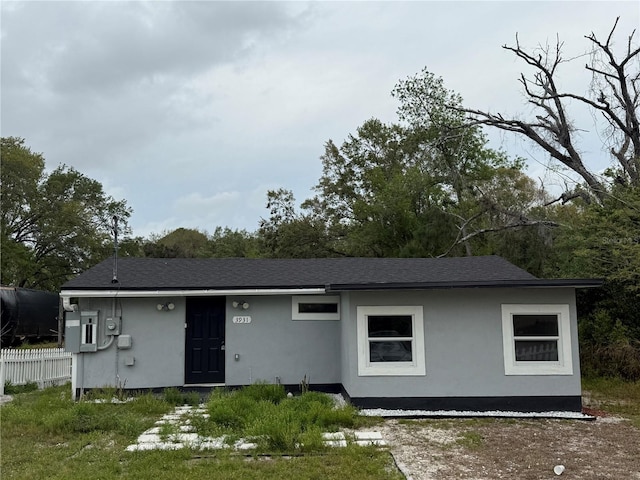 view of front of house featuring stucco siding, roof with shingles, and fence