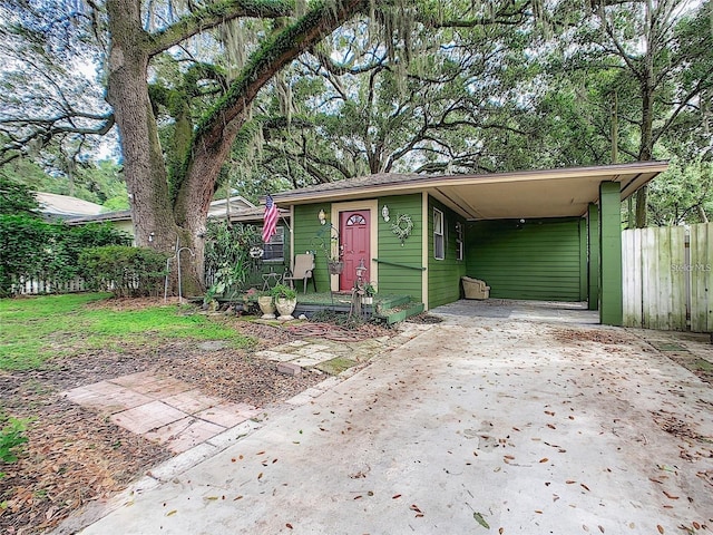 view of front of home with concrete driveway, a carport, and fence