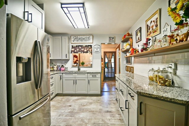 kitchen featuring a sink, backsplash, light stone countertops, and stainless steel fridge with ice dispenser