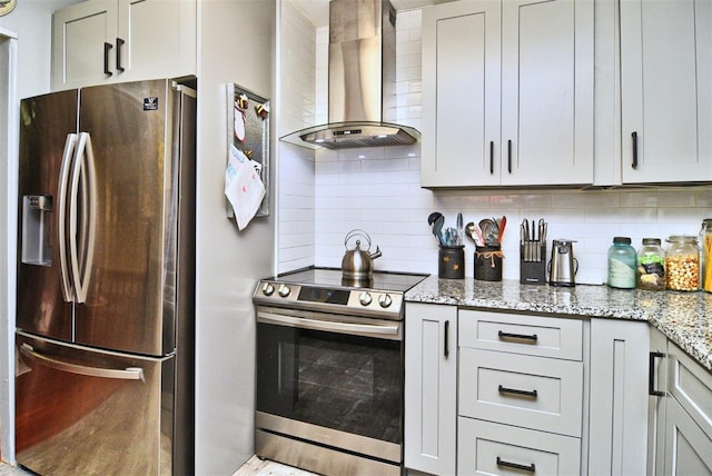 kitchen with backsplash, light stone counters, gray cabinets, appliances with stainless steel finishes, and wall chimney exhaust hood