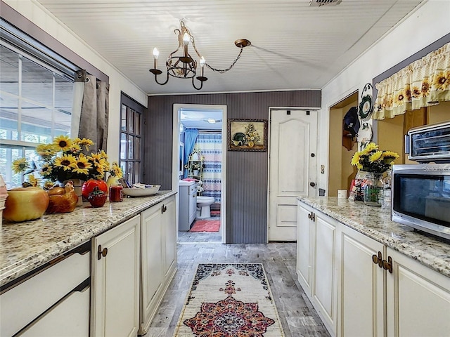 kitchen with stainless steel microwave, light stone countertops, light wood-type flooring, an inviting chandelier, and white cabinetry