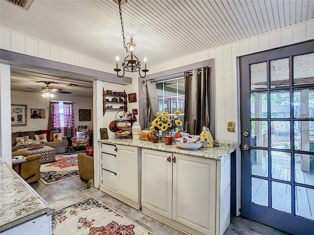 kitchen featuring ceiling fan with notable chandelier, decorative light fixtures, light stone counters, open floor plan, and white cabinetry