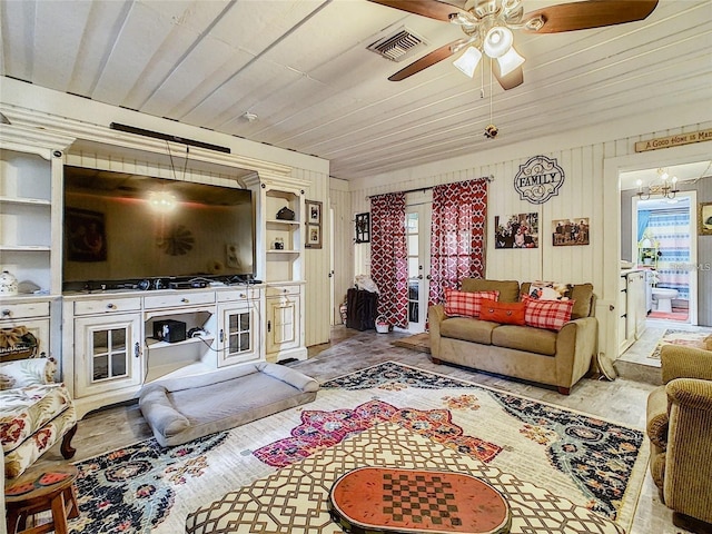 living room with visible vents, wooden ceiling, wood walls, and ceiling fan with notable chandelier