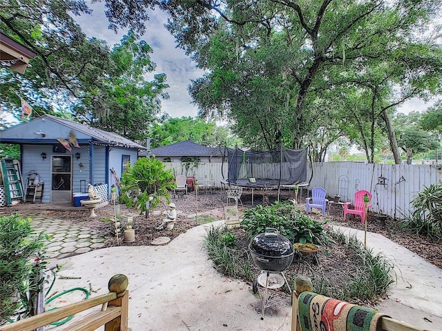 view of yard with a patio, an outdoor structure, a trampoline, and fence