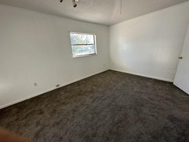 spare room with dark colored carpet, baseboards, and a textured ceiling