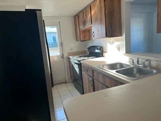 kitchen with black range with electric cooktop, light countertops, light tile patterned floors, freestanding refrigerator, and a sink