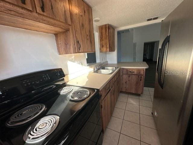 kitchen featuring black range with electric cooktop, freestanding refrigerator, light tile patterned flooring, brown cabinetry, and a sink