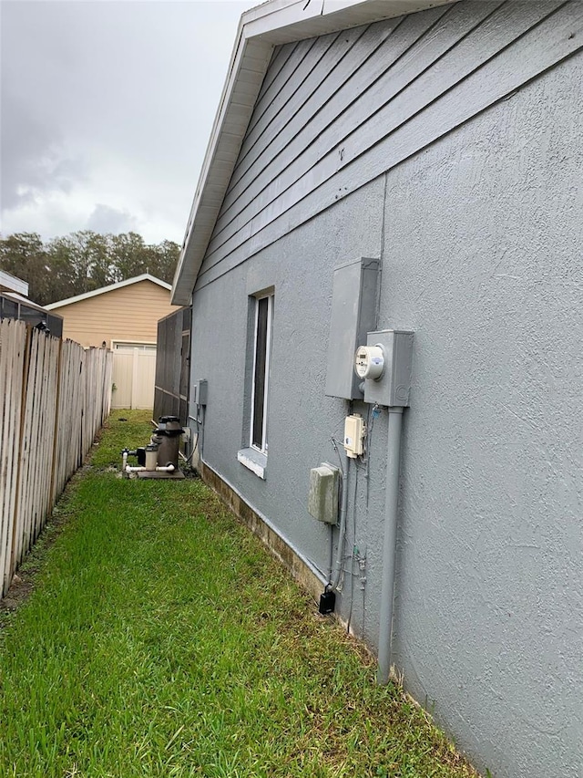 view of property exterior with stucco siding, a lawn, and fence